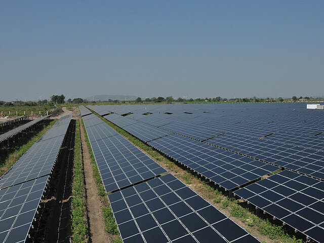 A large solar plant stands on an open field and produces a lot of electricity in bright sunshine.